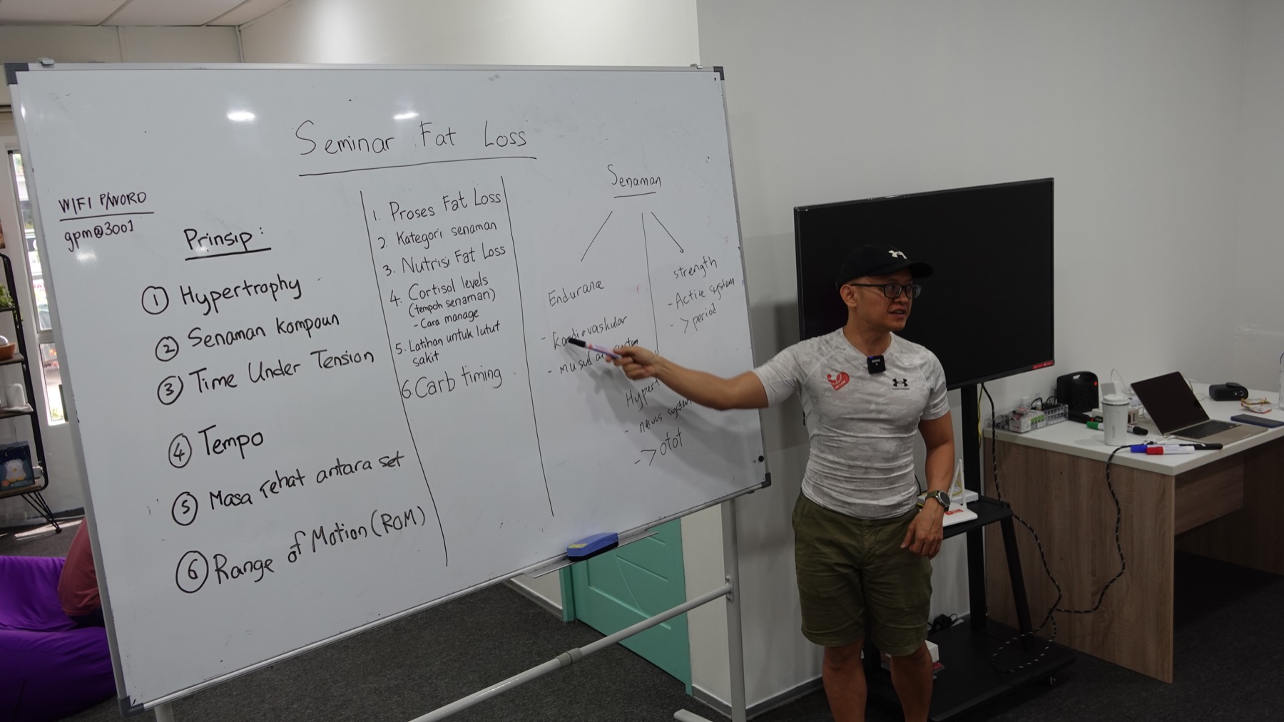 Coach Ho explaining fat-loss principles beside a seminar whiteboard